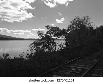 Black And White Shot Of Serene Silver Lake With Railroad Tracks, Clouds & Trees In View, Madison New Hampshire