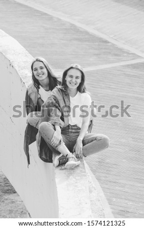 Black and white shot of Two young women in white shirt and jeans sitting and laughing together