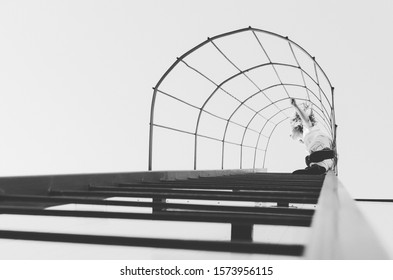 Black And White Shot Of Woman Climbing Ladder On A Roof