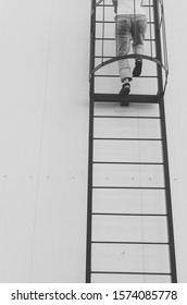 Black And White Shot Of Woman Climbing Ladder On A Roof