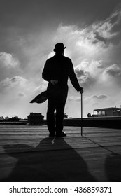 Black and white silhouette of an elegant gentleman on a rooftop with a cane, wearing a long a coattail and a bowler hat