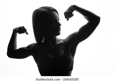 Black and white silhouette girl athletes posing on a white background, showing his sports beefy body, muscles in his arms. The dark silhouette of a sportswoman with beautiful pumped biceps in a Studio