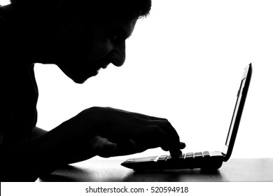 black and white silhouette of a hacker typing on the keyboard of laptop remotely hacking and receiving personal information