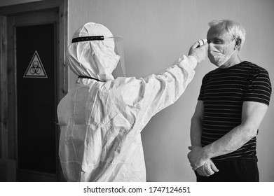 Black And White Snapshot Of Doctor's Visit At Patient's Home During Quarantine 2020. Rear View Image Of Doctor Measuring Old Man's Fever With Infrared Contactless Thermometer. Coronavirus Concept