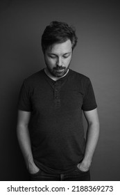 Black And White Studio Portrait Of A 40 Year Old Caucasian Man. He Is Looking Down And Is Wearing A Dark Shirt And Jeans.