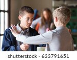 Black and white teenage male students fighting indoors. Obscured teacher in background.