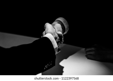 Black and white tone of anonymous business partners making handshake in dark shadow