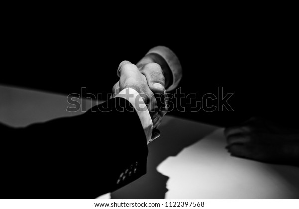 Black and white tone of anonymous business\
partners making handshake in dark\
shadow