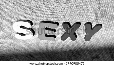 Black and white top down view of the word SEXY spelled with wooden puzzle letters on textured background