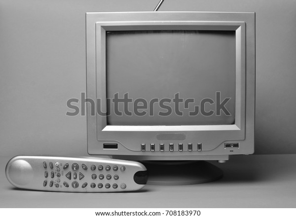 Black and white TV and remote control\
close-up on a wall\
background.