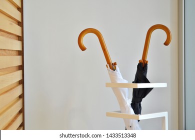 Black And White Umbrella Stand In Special Geometric Stand Against The White Wall And Wooden Stand Indoors