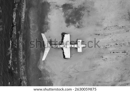 Black and white version of top-down drone shot showing the silhouette of the Lun-class ekranoplan resting on a wide sand patch by the sea.