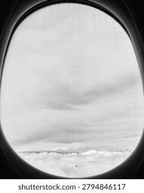 Black and white view of clouds through an airplane window, with a rounded aircraft porthole framing the sky in a minimal travel and aviation composition.