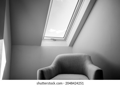 Black and white view of a newly installed loft conversion showing a modern fabric seat in a bedroom location. A skylight window is seen also.