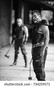 Black and white view of two aggressive men in leather armor, weapon and metal spiked mask on their faces berore fight inside old abandoned building 