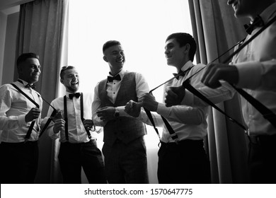 Black And White Wedding Photography. Groom Smiling When Groomsmen Pull Up The Suspenders