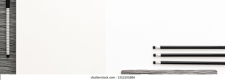 A Black And White Work Desk. Opened Notebook, Pencils In A Row And Empty Space For Text. Copy Space And Mockup. Panoramic Top View. Monochromatic Pattern. 