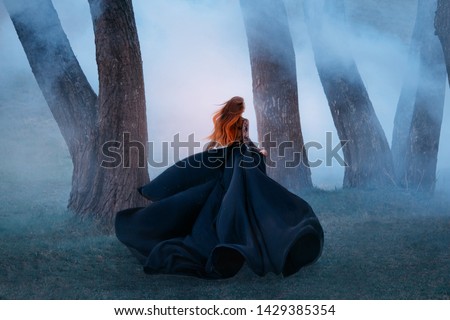 black widow long dark silk fly fabric dress, scary horror woman red hair runs mystery forest turned away black lady night walk gothic blue fog nature tree. art photo shoot mysterious woman silhouette