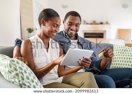 Black wife doing shopping online while using digital tablet at home with husband. Couple using bank card to pay bills or to book their next vacation. Mature couple making an online purchase.