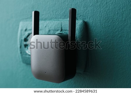 Black WiFi repeater in electric socket on green wall