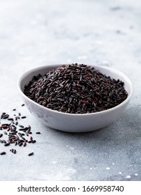 Black wild rice in a bowl. Grey background. Close up.