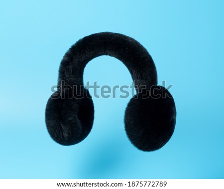 Black winter fur earmuffs on blue background. Minimal fashion concept.
