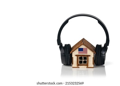 Black Wireless Headphones On A Small Wooden House And The US Flag. Music Concept. House Soundproofing Concept. Copy Space.