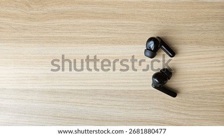 Black wireless headset or earphone is called TWS (true wireless stereo) without the charging case, isolated on wooden table background. Flat lay and close up.