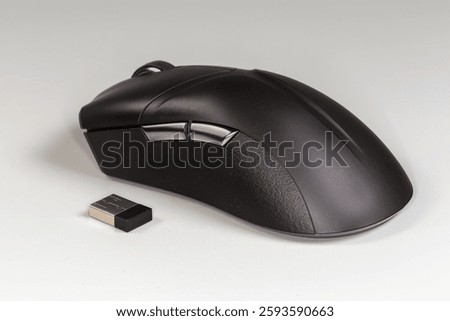 Black wireless optical computer mouse with scroll wheel and additional side buttons and its USB receiver on a gray background, side view close-up in selective focus
