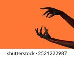 Black witch hands with claws on orange background. Halloween celebration