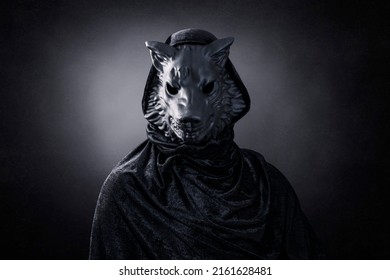 Black wolf in hooded cloak at night over dark misty background