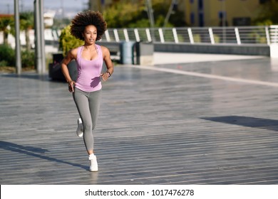 Black woman, afro hairstyle, running outdoors in urban road. Young female exercising in sport clothes. - Powered by Shutterstock