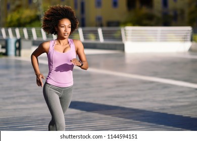 Black woman, afro hairstyle, running outdoors in urban road. Young female exercising in sport clothes. - Powered by Shutterstock