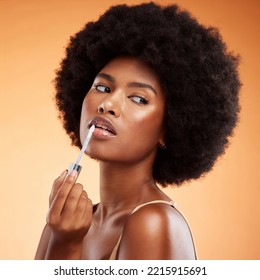 Black woman, afro and natural beauty lip gloss treatment for a healthy, shiny and transparent tint. Cosmetics, apply and beautiful face of African model holding makeup tool at orange background. - Powered by Shutterstock