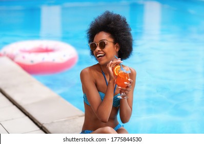 Black woman in bikini with delicious cocktail resting by pool outside