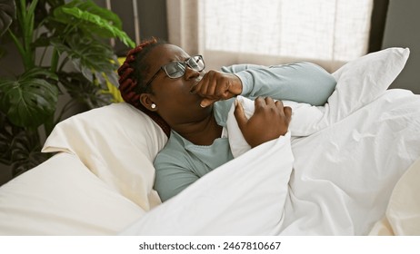 A black woman with braids coughing in bed, depicting illness in a home interior setting. - Powered by Shutterstock