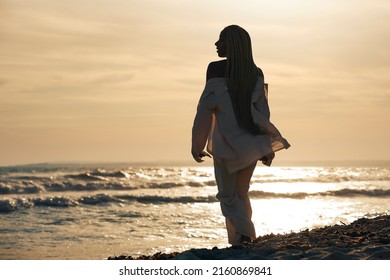 Black Woman With Braids Walking On The Beach Barefoot, Spending The Vacation In The Sunset With Her Back Turned. Horizontal Photo