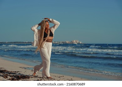 Black Woman With Braids Walking On The Beach In Summer With A Wide Beach Outfit. With A Happy Expression. Walking Barefoot