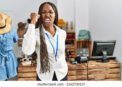 Black woman with braids working as manager at retail boutique angry and mad raising fist frustrated and furious while shouting with anger. rage and aggressive concept. 