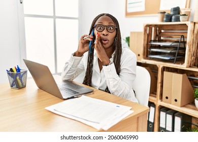 Black Woman With Braids Working At The Office Speaking On The Phone Hand On Mouth Telling Secret Rumor, Whispering Malicious Talk Conversation 