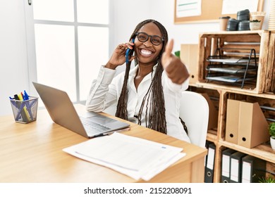 Black Woman With Braids Working At The Office Speaking On The Phone Approving Doing Positive Gesture With Hand, Thumbs Up Smiling And Happy For Success. Winner Gesture. 