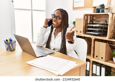 Black Woman With Braids Working At The Office Speaking On The Phone Pointing Fingers To Camera With Happy And Funny Face. Good Energy And Vibes. 