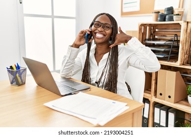 Black Woman With Braids Working At The Office Speaking On The Phone Smiling Doing Phone Gesture With Hand And Fingers Like Talking On The Telephone. Communicating Concepts. 