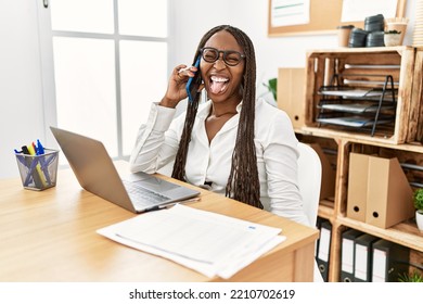 Black Woman With Braids Working At The Office Speaking On The Phone Sticking Tongue Out Happy With Funny Expression. Emotion Concept. 