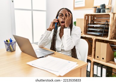 Black Woman With Braids Working At The Office Speaking On The Phone Yawning Tired Covering Half Face, Eye And Mouth With Hand. Face Hurts In Pain. 