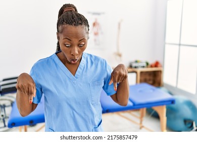 Black Woman With Braids Working At Pain Recovery Clinic Pointing Down With Fingers Showing Advertisement, Surprised Face And Open Mouth 