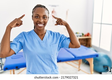 Black Woman With Braids Working At Pain Recovery Clinic Smiling Pointing To Head With Both Hands Finger, Great Idea Or Thought, Good Memory 