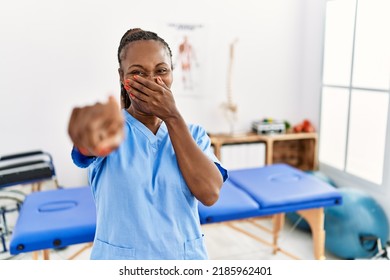 Black Woman With Braids Working At Pain Recovery Clinic Laughing At You, Pointing Finger To The Camera With Hand Over Mouth, Shame Expression 