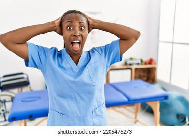 Black Woman With Braids Working At Pain Recovery Clinic Crazy And Scared With Hands On Head, Afraid And Surprised Of Shock With Open Mouth 