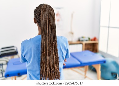 Black Woman With Braids Working At Pain Recovery Clinic Standing Backwards Looking Away With Crossed Arms 